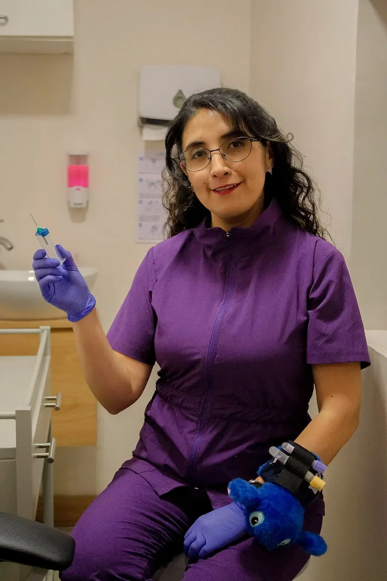 Bioquímica sonriendo con un tubo de muestra en la mano, sentada en la sala de toma de muestras
