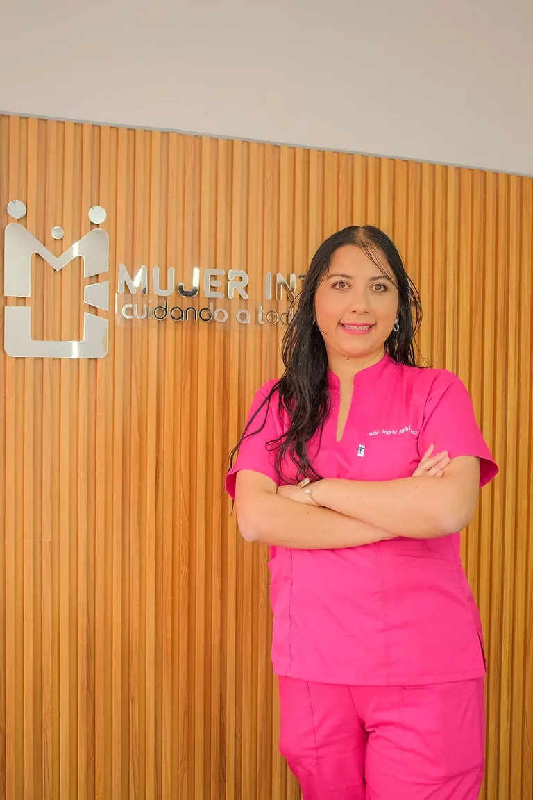 Bioquímica con uniforme fucsia, de pie con los brazos cruzados junto al rótulo Mujer Integral